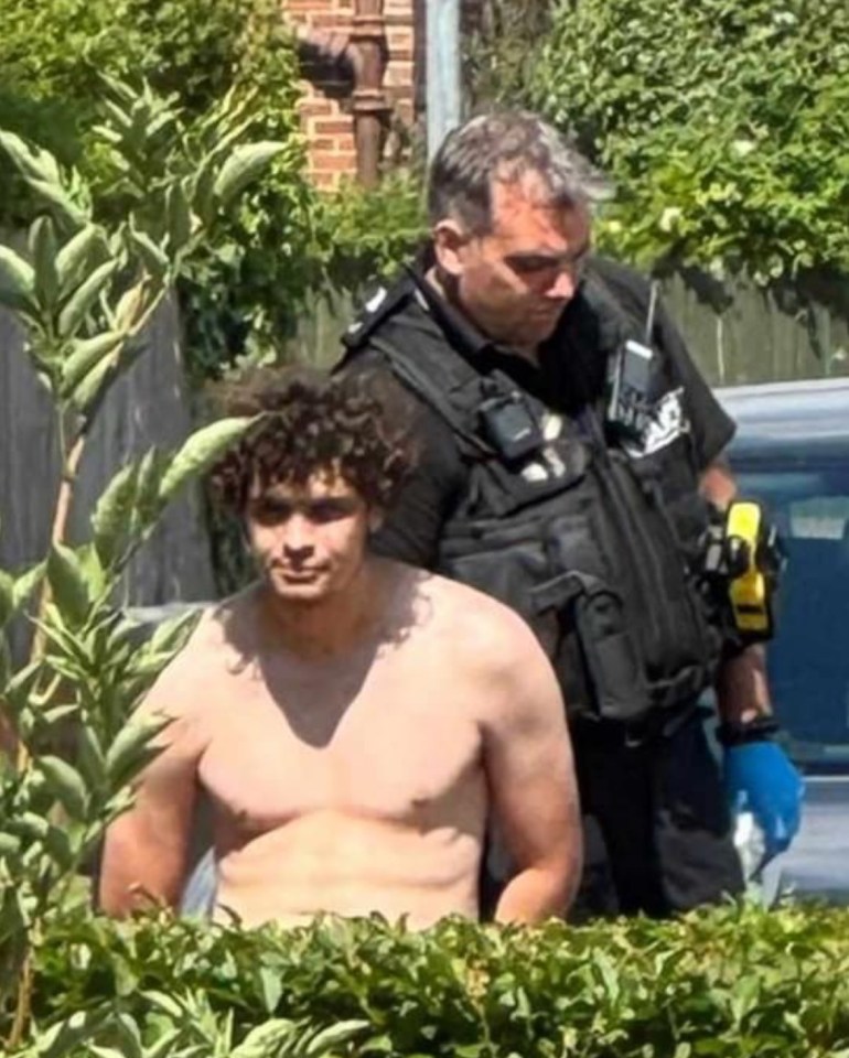 Logan Burnett, shirtless, under arrest by a police officer.