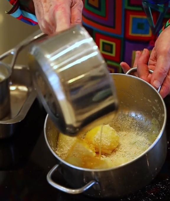 Person adding liquid to potatoes and breadcrumbs in a pan.