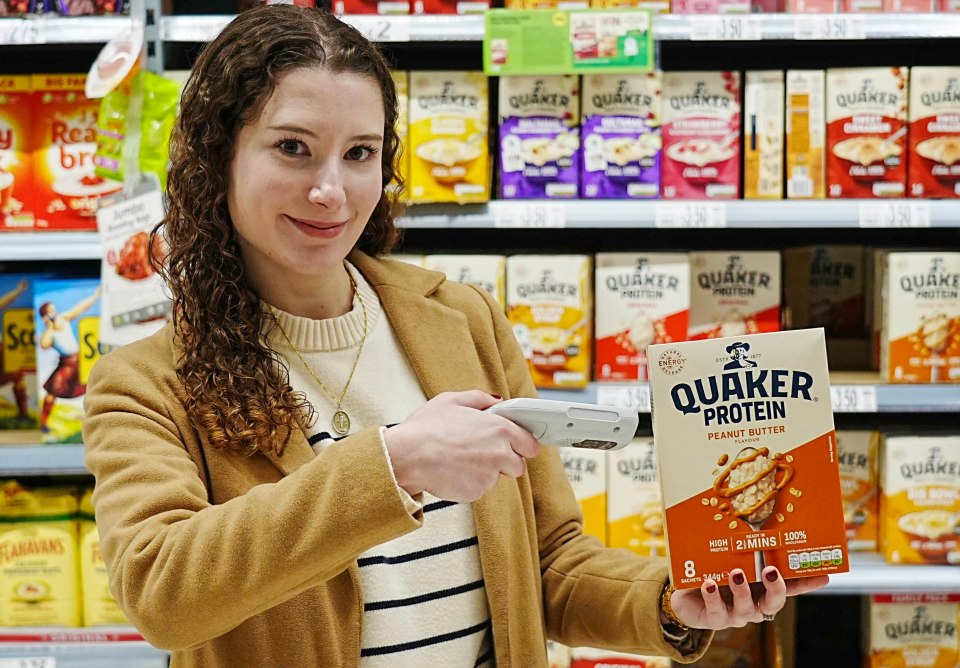 Woman scanning a box of Quaker Protein Peanut Butter flavored oatmeal in a grocery store.