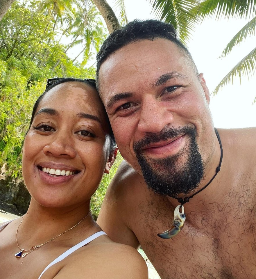 Couple smiling for a selfie in front of palm trees.