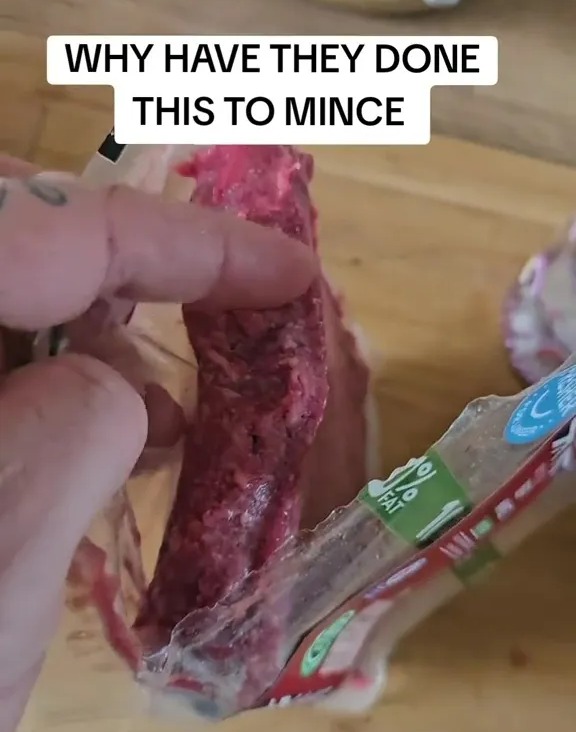 Hand holding a package of ground beef that is clumped together.