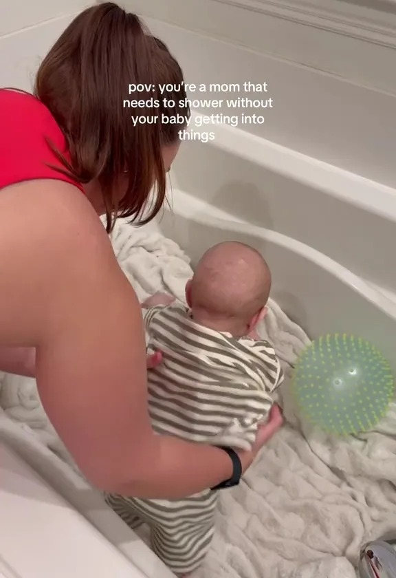 Mom showering while baby plays safely in the bathtub.