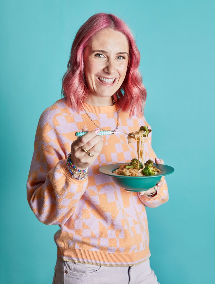 Woman with pink hair eating gluten-free pasta with broccoli.