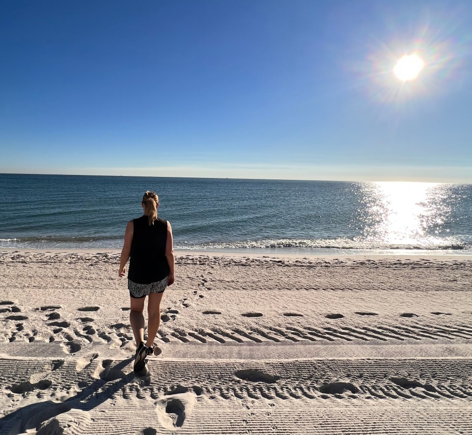 Woman walking away from the camera on a sunny beach.