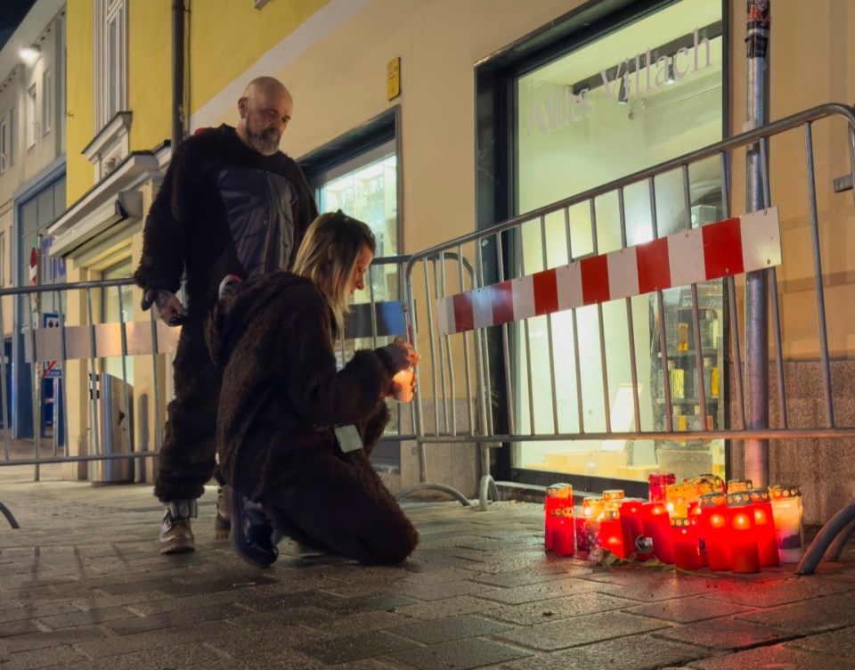 Two people light candles at a memorial.