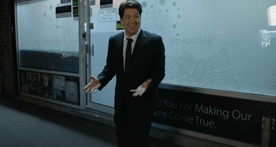 Man in suit gesturing in front of a storefront.