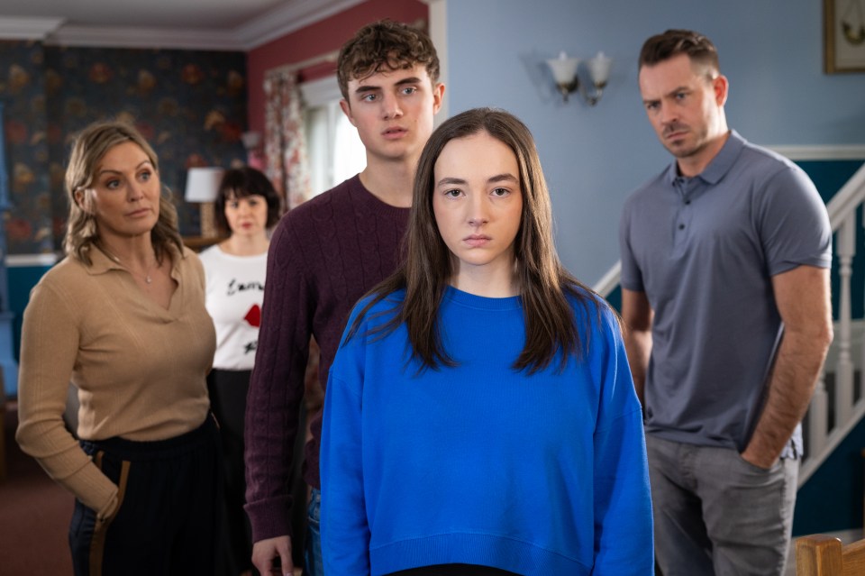 A teenage girl stands in front of her family.