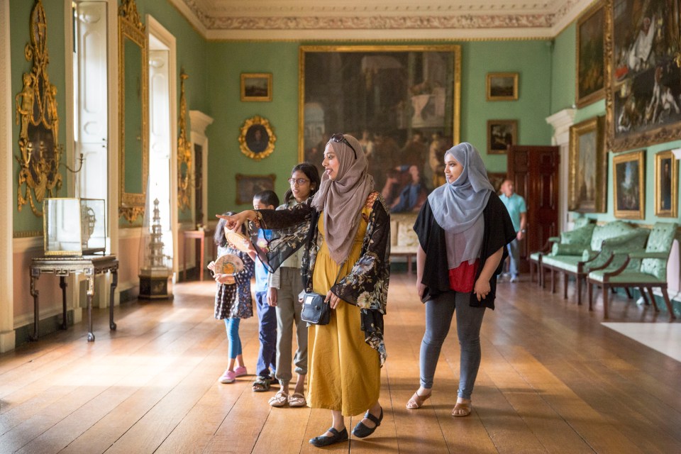 A woman points out artwork in a grand room to a group of children and another woman.