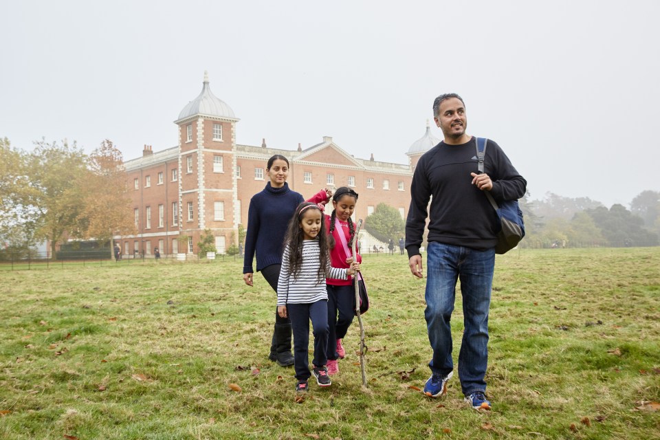 Family walking on a grassy field in front of a large brick building.