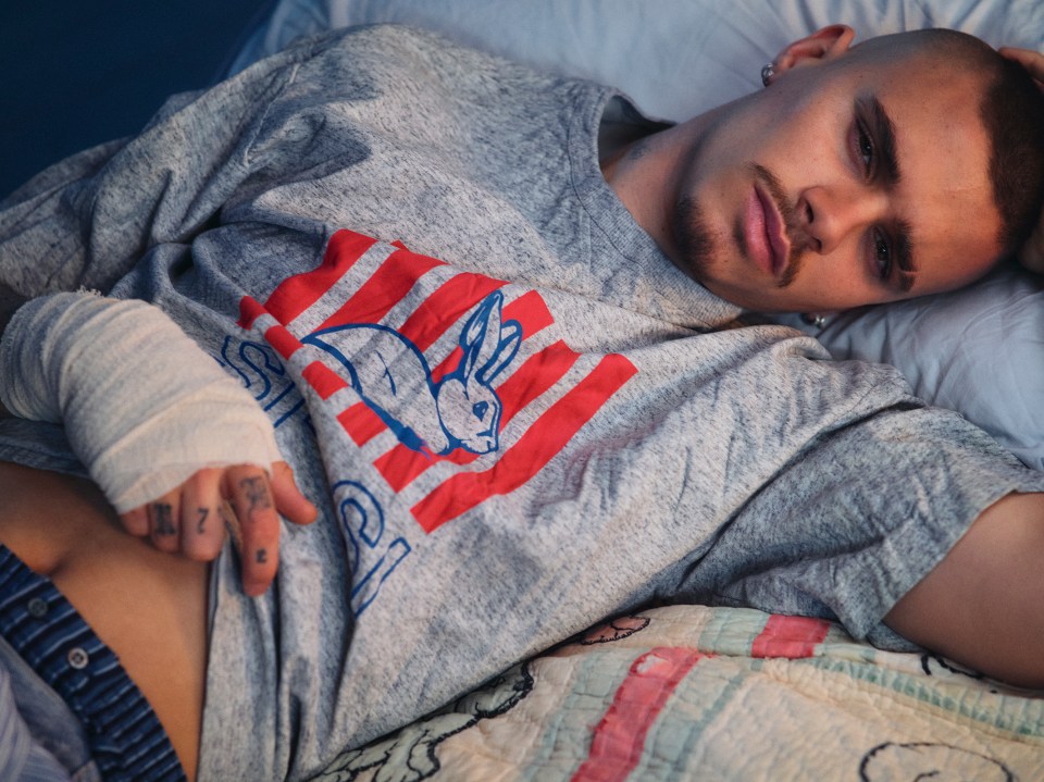 Man with bandaged hand lying on bed wearing gray shirt with rabbit graphic.