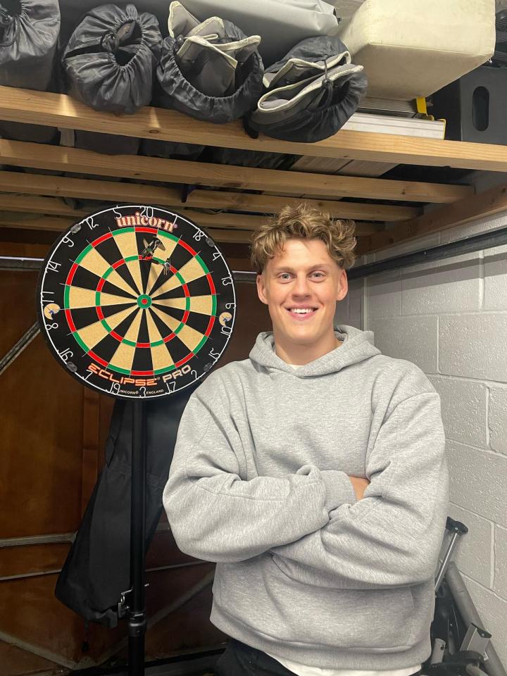 Man standing with arms crossed in front of a dartboard.
