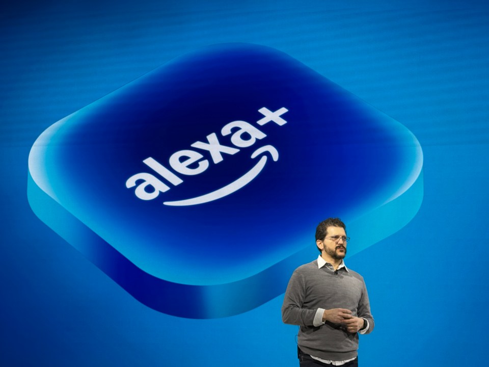 A man stands in front of a large blue Alexa+ logo.
