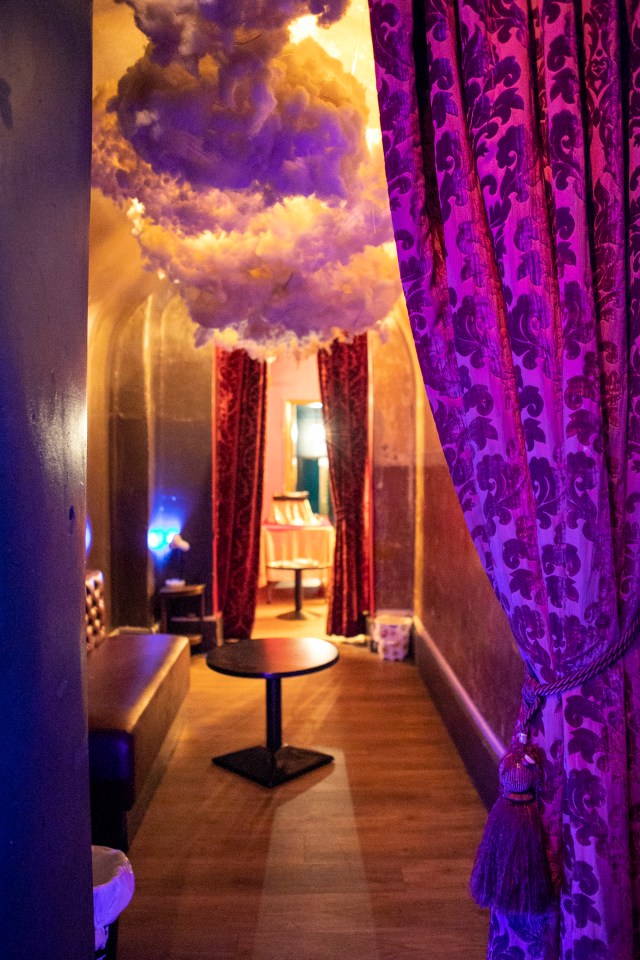 Interior view of a dimly lit bar area with purple curtains and a cloud-like ceiling fixture.
