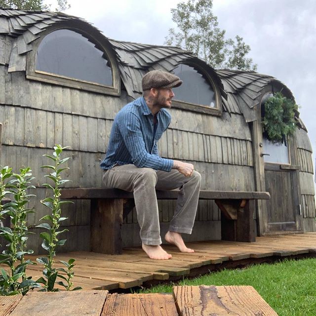 David Beckham sitting barefoot on a bench outside a wooden sauna.