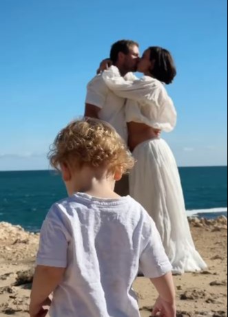 Toddler watching parents kiss by the ocean.