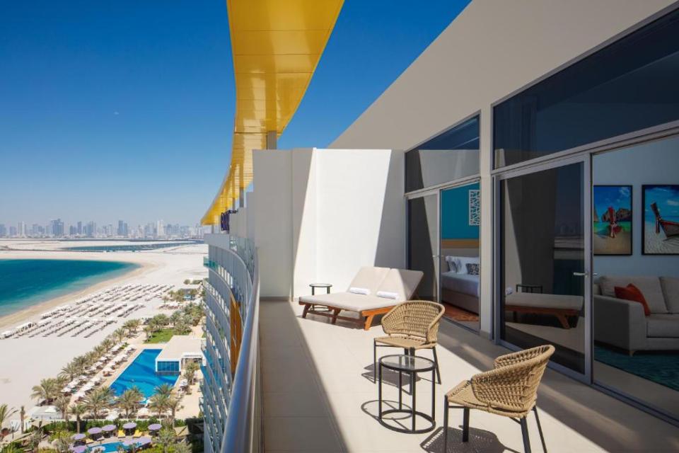 Balcony overlooking beach and city with lounge chairs and small table.