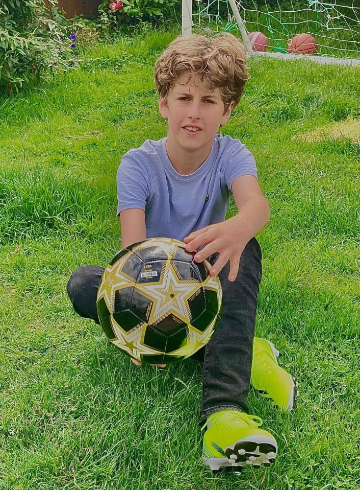Boy sitting on grass holding soccer ball.