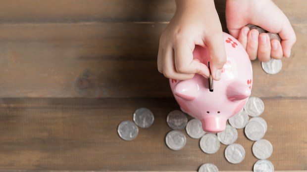 a child is putting coins into a pink piggy bank
