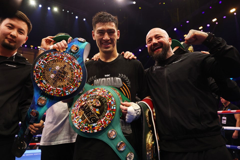 Dmitrii Bivol celebrating a boxing victory with championship belts.