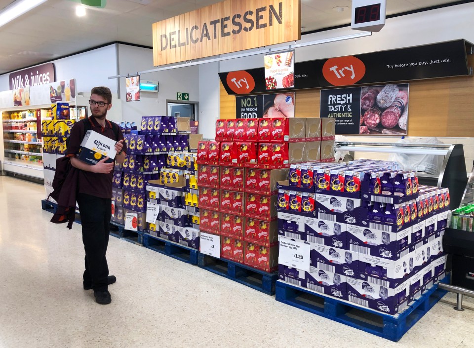 A man in a supermarket holds a box of Corona beer while standing near displays of Easter eggs.