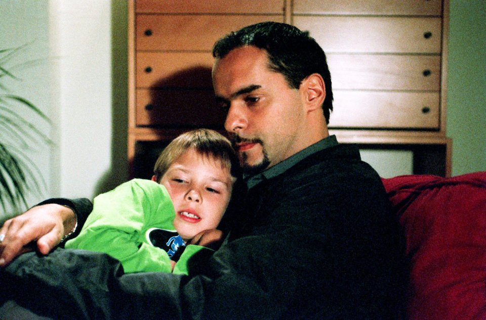A man and young boy cuddling on a couch.