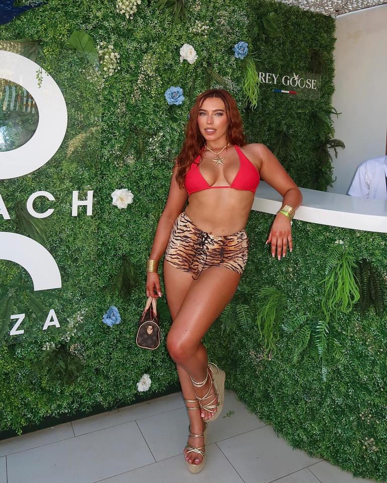 Woman in red bikini top and animal print shorts posing in front of a green wall.