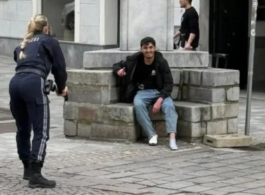 Police officer approaching a man sitting on a low stone wall.