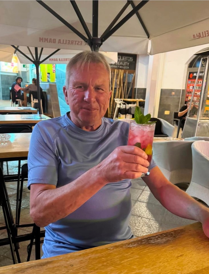 A man holds a cocktail at an outdoor cafe.