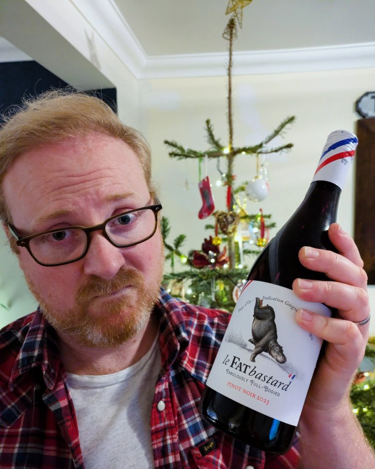 Man holding a bottle of Le Fat Bastard Pinot Noir in front of a Christmas tree.