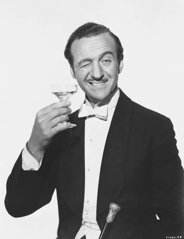 Man in tuxedo winking and holding a cocktail glass.