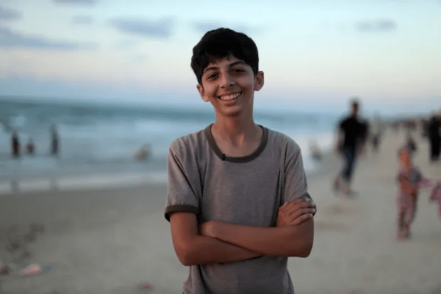 Smiling boy with arms crossed on a beach.