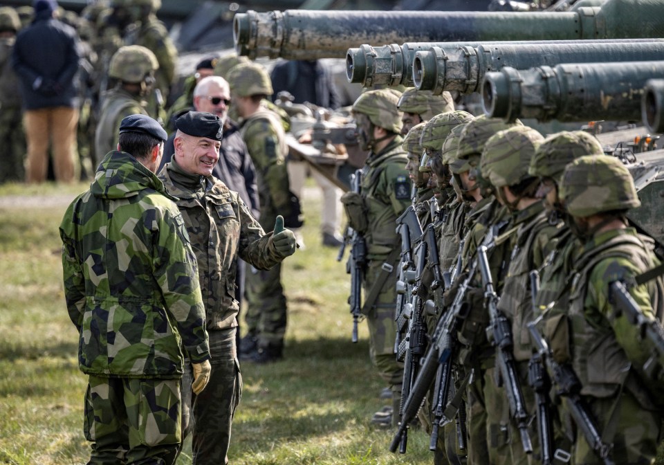 A man in military uniform gives a thumbs-up to a line of soldiers.