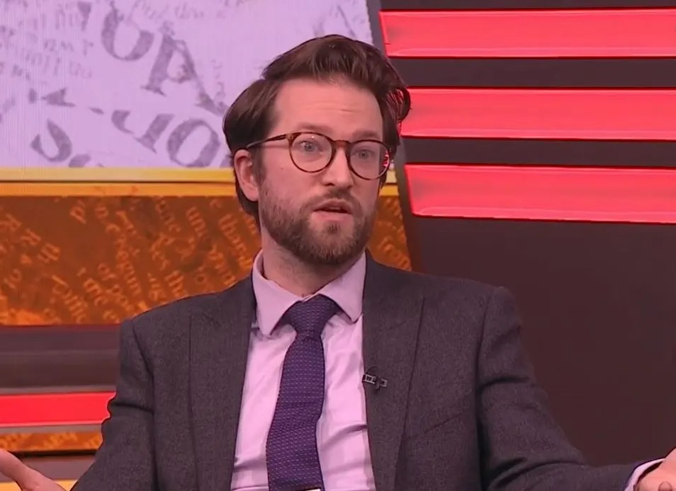 Man in suit and glasses speaking.