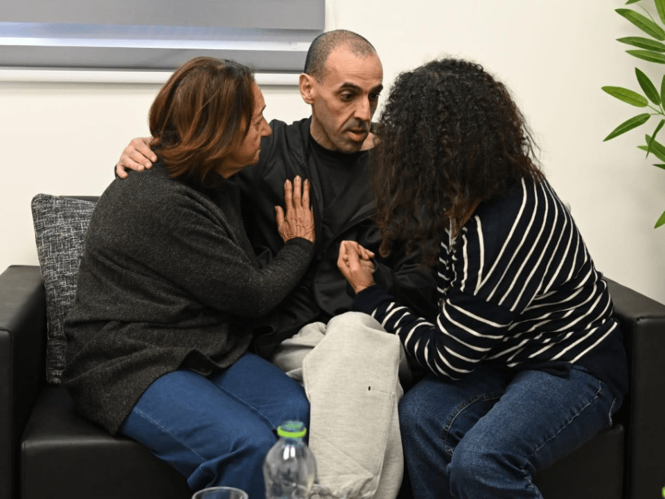 A man sitting on a couch comforted by two women.