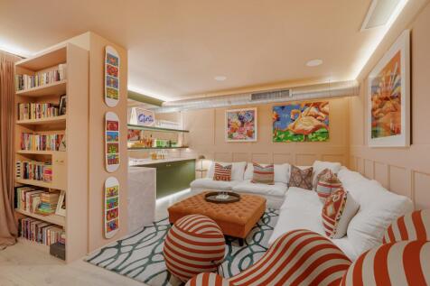 Interior view of a living room with a large white sectional sofa, orange and white striped armchairs, and artwork on the walls.