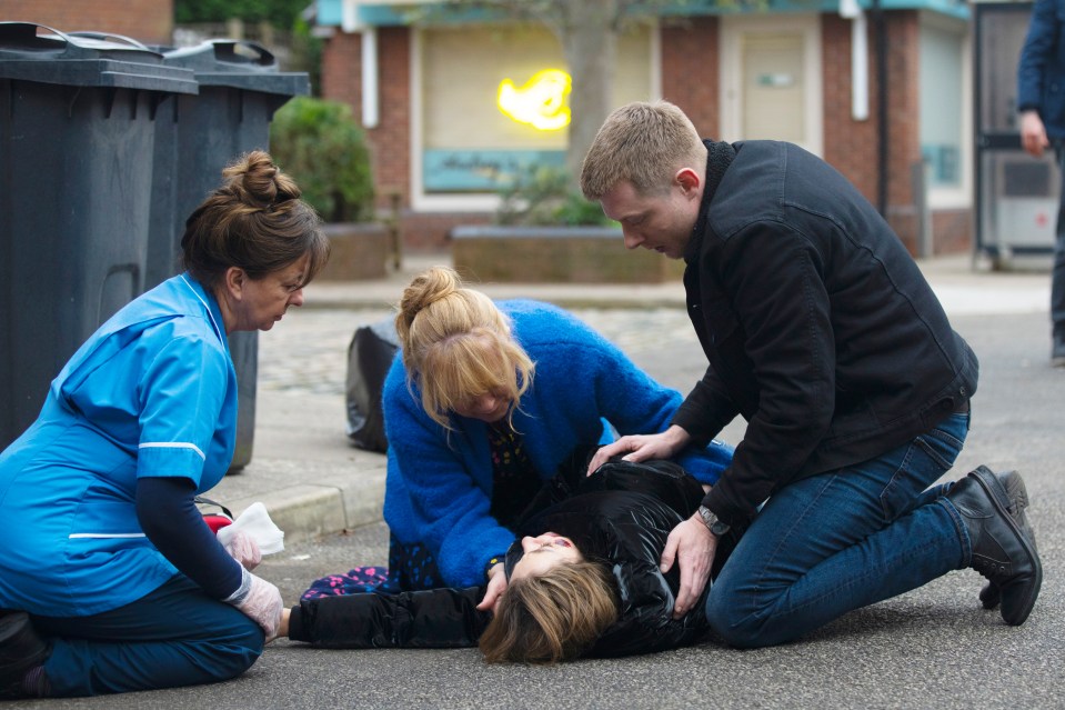 A woman lies injured on the ground as several people attend to her.