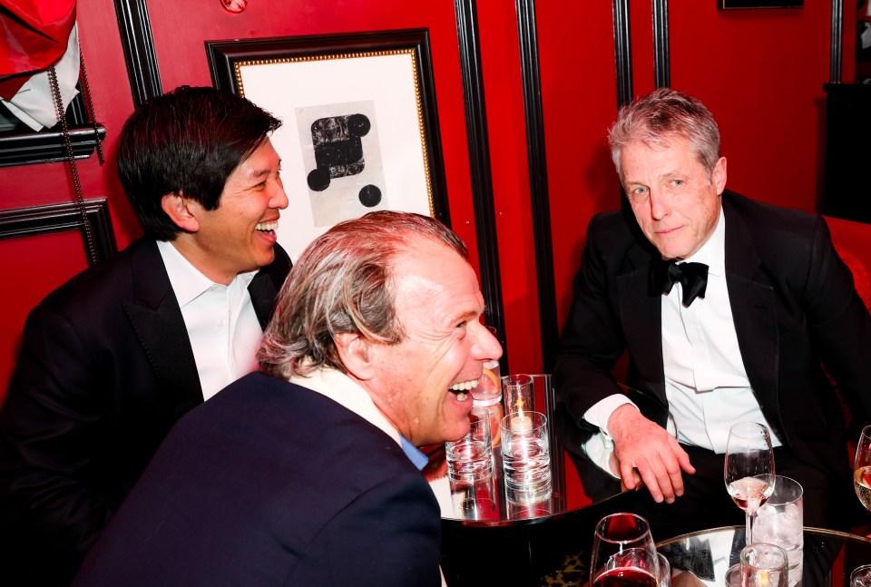 Three men in suits laughing at a table.