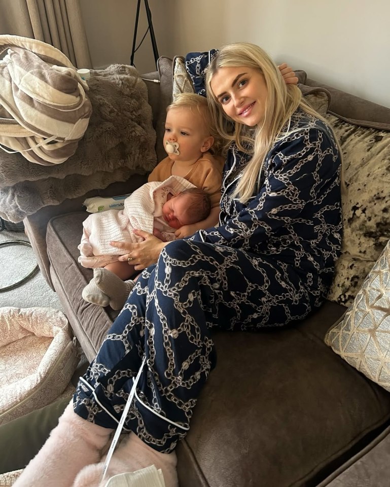 Woman in pajamas holding two babies on a couch.