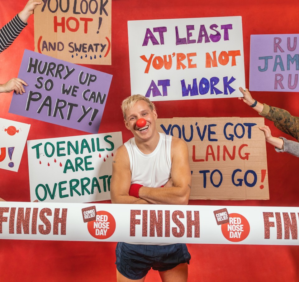 Jamie Laing, holding a finish line banner for Red Nose Day, surrounded by supportive signs.