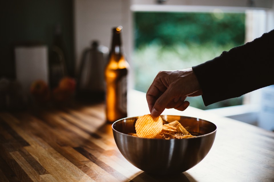A person's hand reaching for potato chips from a bowl.