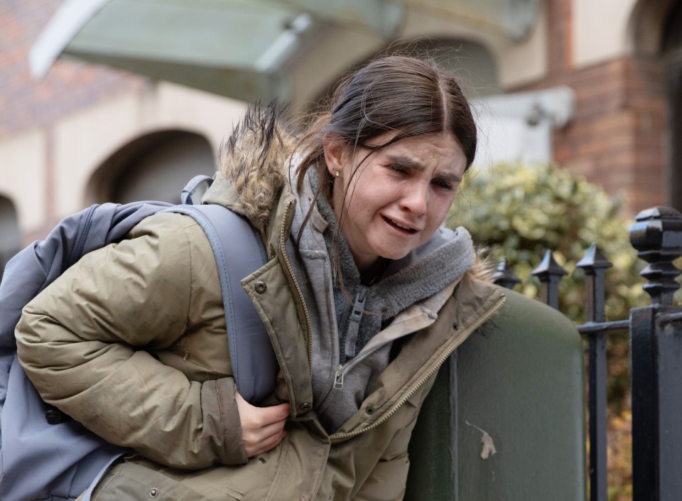A young woman crying while leaning against a fence.