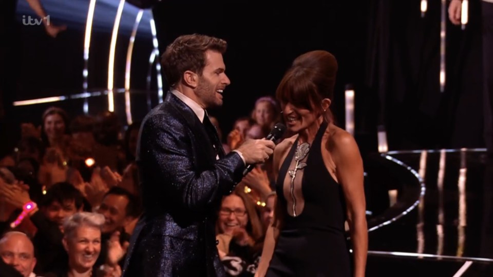 Two Masked Singer hosts on stage with an audience.