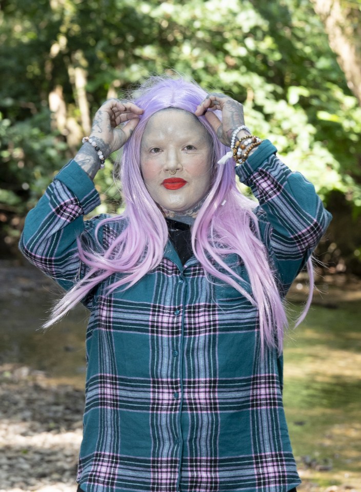 Portrait of Melissa Sloan, a heavily tattooed woman with lavender hair, wearing a teal plaid shirt.