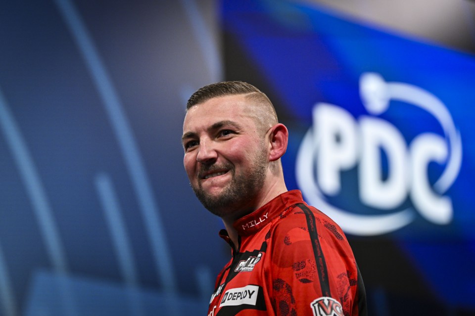 Nathan Aspinall smiling after winning a darts match.