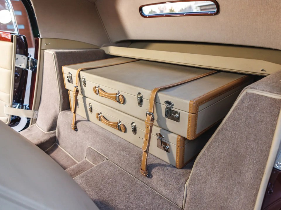 Two tan leather suitcases in the trunk of a classic car.