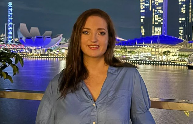 Woman in blue shirt in front of Singapore skyline at night.