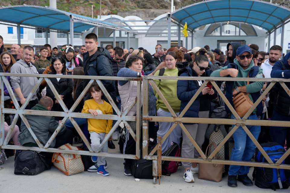 People waiting behind a fence at a ferry port.