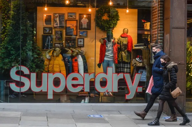 People wearing face masks walk past a Superdry store.
