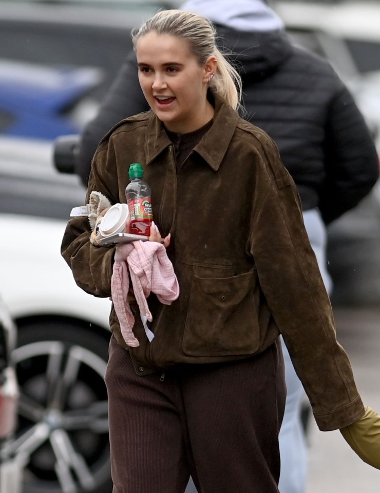 Woman carrying a drink, a stuffed animal, and a pink cloth.