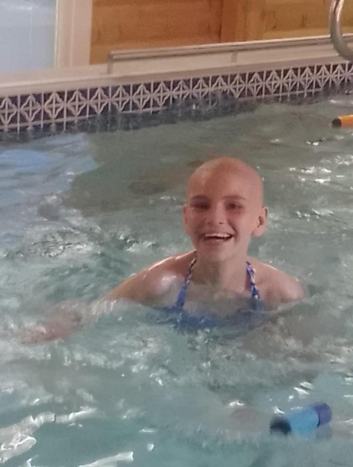 A smiling bald girl in a swimming pool.